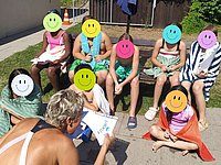 Kinder in Badebekleidung, unkenntlich durch Smiley auf dem Gesicht, bekommen eine Schwimmurkunde überreicht