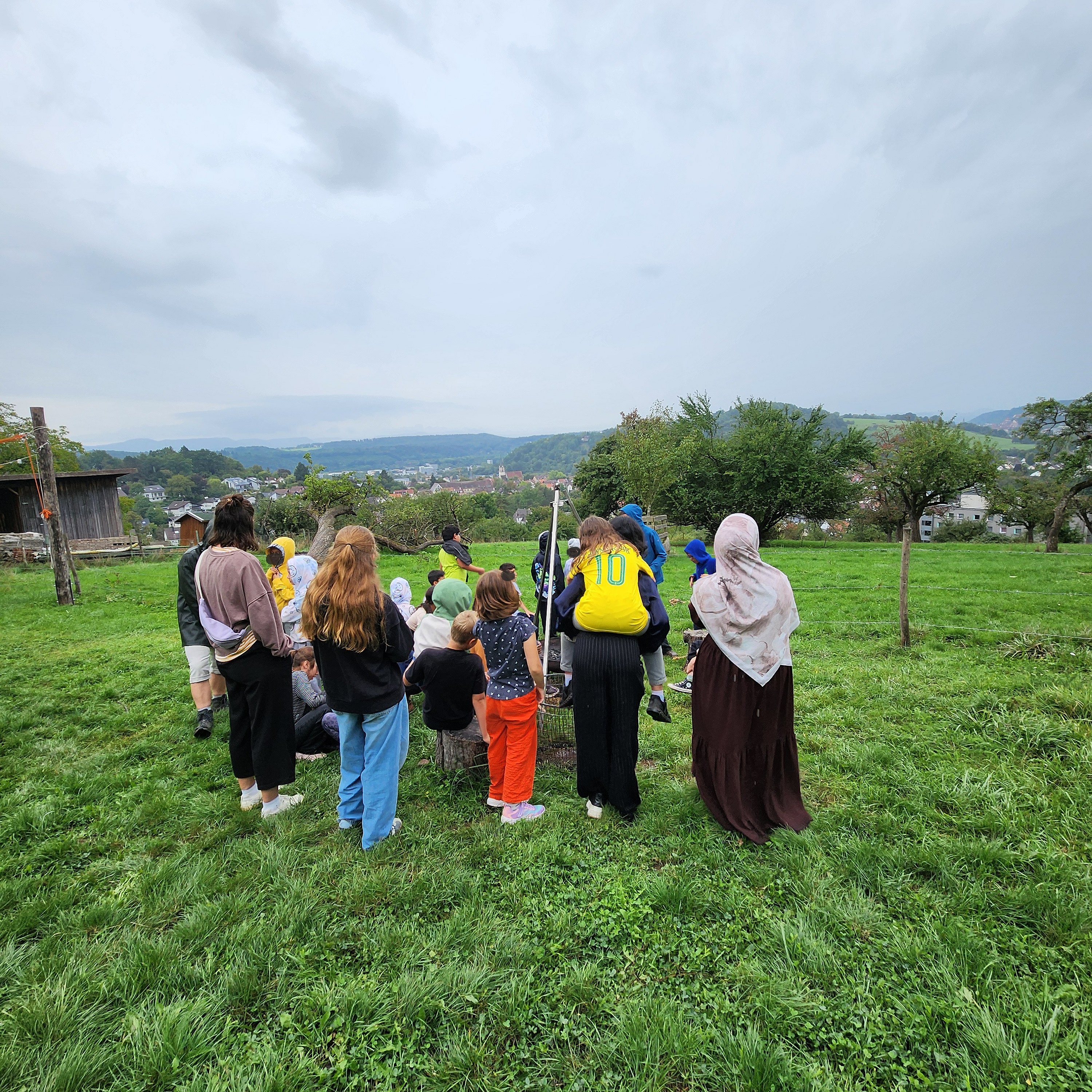 Gruppe von Kindern und Betreuern auf einem Feld, mit dem Rücken zum Betrachter stehend