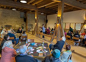 Menschen im Veranstaltungsraum in einer umgebauten Scheune, auf den Tischen und an den Wänden Moderations- und Themenkarten