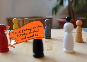 Spielfiguren auf einem Holzbrett - Text in Sprechblase: Sozialpädagogische studentische Hilfskräfte