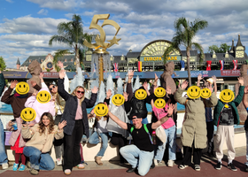 Gruppe von Kindern mit Betreuer:innen vor einem Brunnen im Europark, alle strecken die Hände in die Luft, die Gesichter der Kinder sind mit "Smileys" unkenntlich gemacht