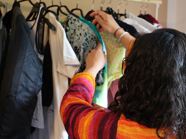 Frau schaut auf einer Kleiderstange hängende Oberteile an