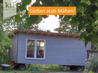 Hellblauer Bauwagen in grüner, bewachsener Umgebung