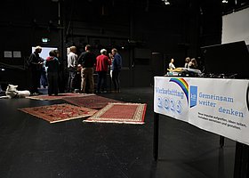 Blick über eine Theaterbühne - im Vordergrund Schilder mit der Aufschrift WERKSTATTTAG 2026 im unscharfen Hintergrund eine kleine Gruppe von Menschen