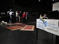 Blick über eine Theaterbühne - im Vordergrund Schilder mit der Aufschrift WERKSTATTTAG 2026 im unscharfen Hintergrund eine kleine Gruppe von Menschen