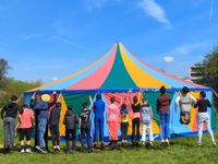 eine Reihe von Kindern springt vor einem bunten Zirkuszelt in die Luft, sie sind von hinten zu sehen