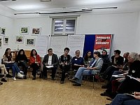 Blick in einen Veranstaltungssaal, viele Menschen sitzen im Kreis, unter ihnen sitzen Kandidierende zur Landtagswahl