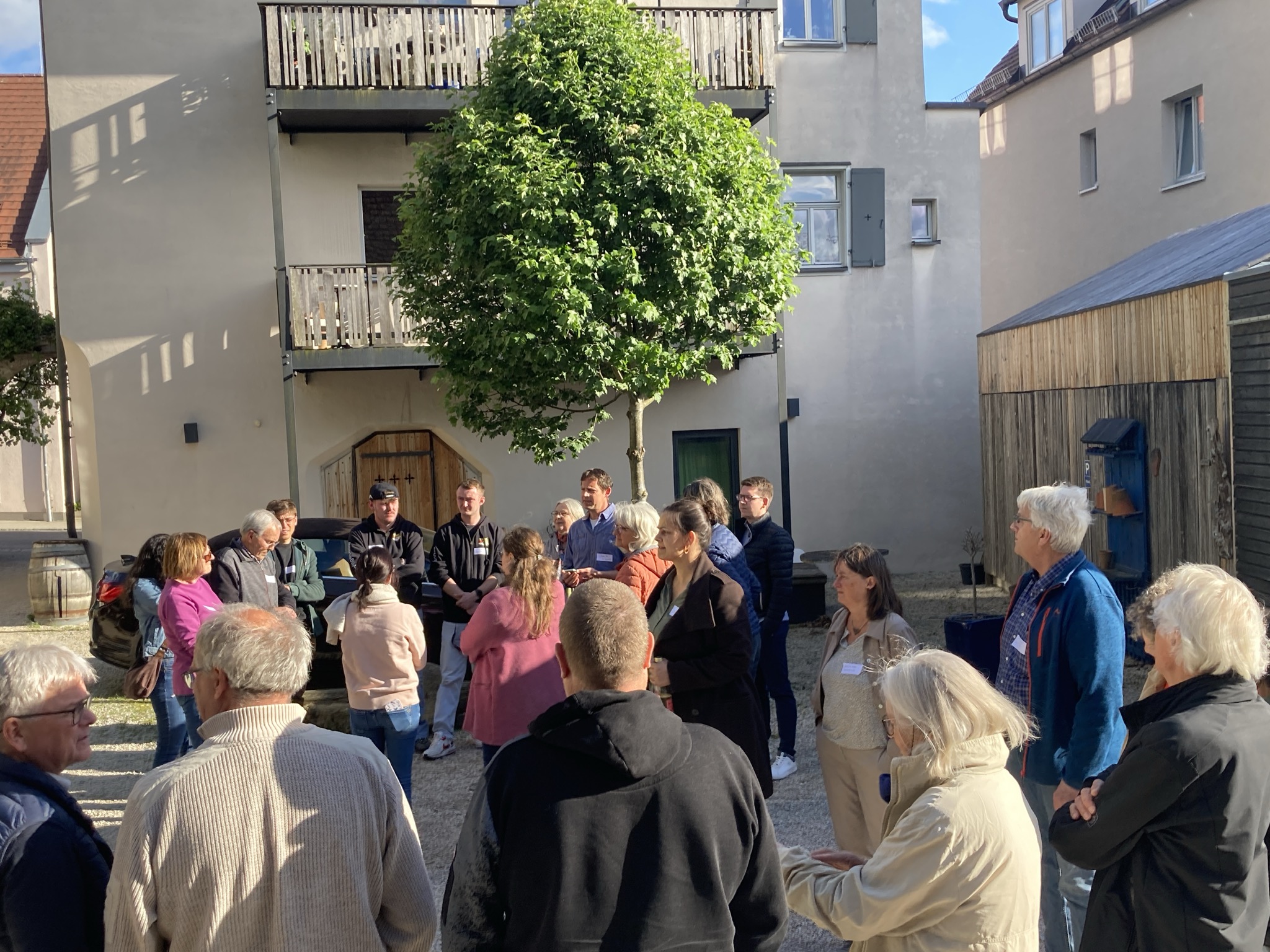 Menschen der Gemeinde stehen im Kreis in einem Innenhof und hören einer Vortragenden zu
