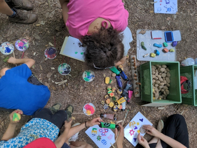 Kinder sitzen draußen auf der Erde und stempeln mit Kartoffeln, von oben fotografiert
