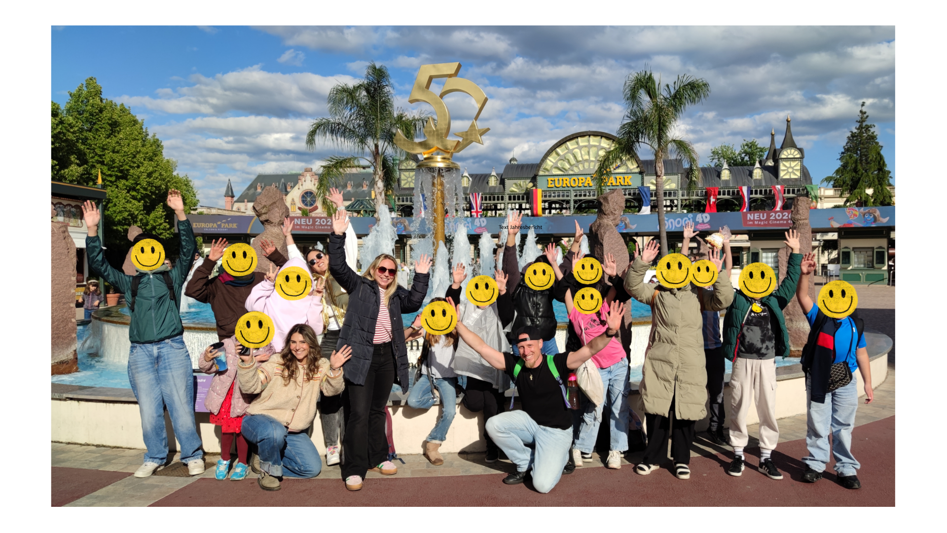 Gruppe von Kindern mit Betreuer:innen vor einem Brunnen im Europark, alle strecken die Hände in die Luft, die Gesichter der Kinder sind mit "Smileys" unkenntlich gemacht